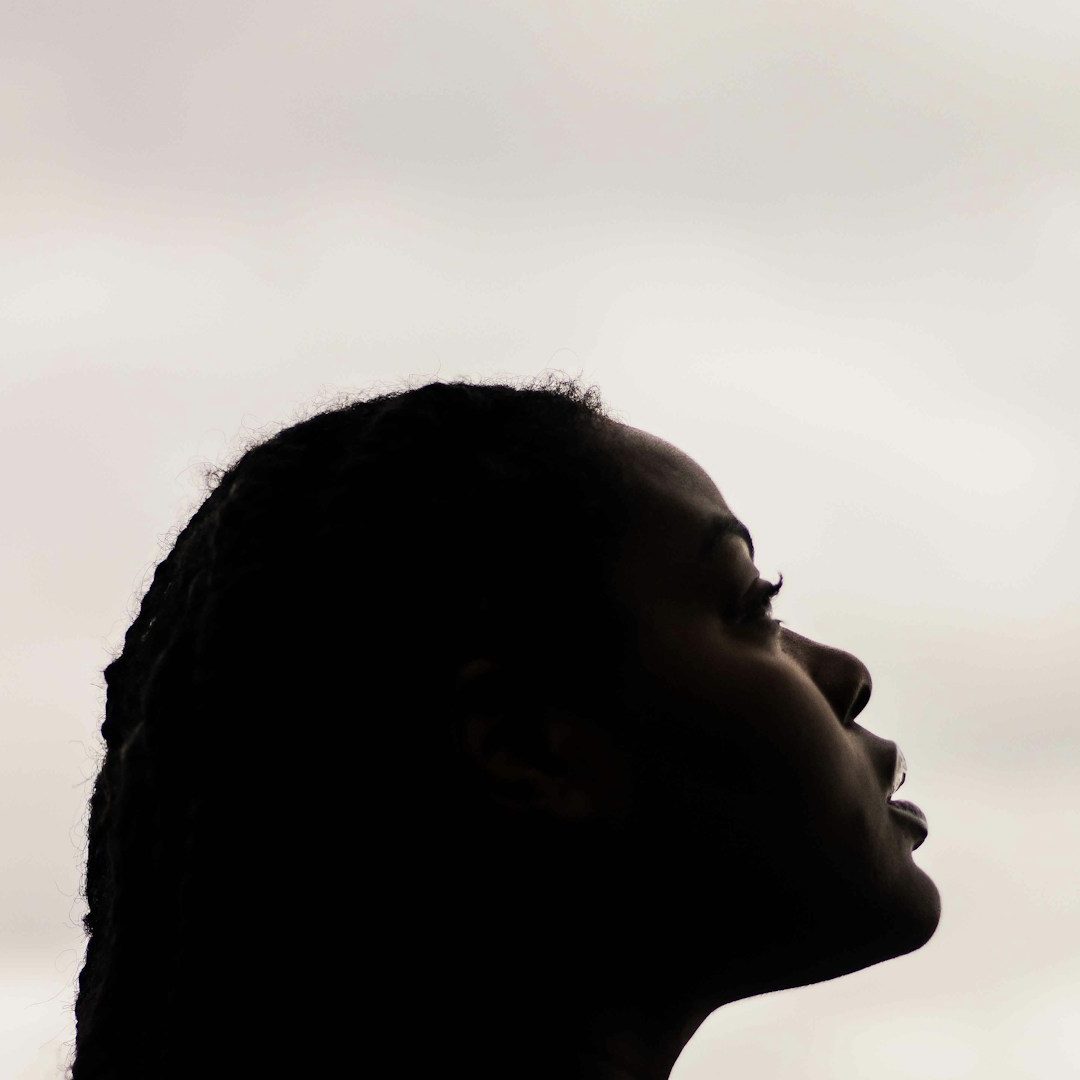 Black Woman Communing with Spirit Profile of a person with braided hair against a cloudy sky.